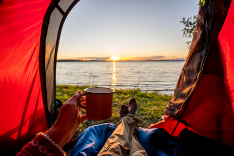 man sitting in tent by the lake with a cup