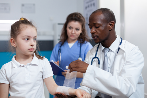 doctor with nurse wrapping bandage around child patient's wrist