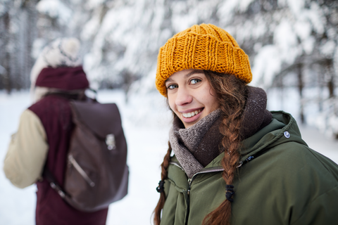 woman with yellow knit cap and braids walking in snow smiling