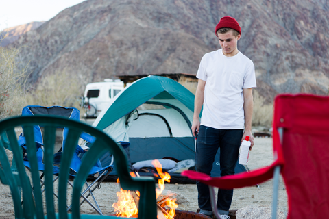 man standing next to campfire in jeans and shirt