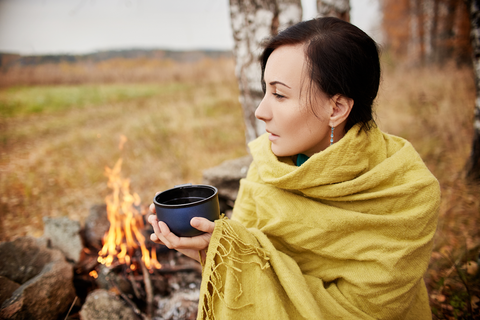 woman wrapped up in a blanket next to camp fire
