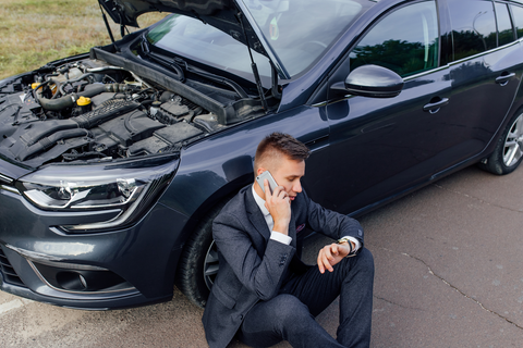 man sitting on road next to car with bonnet open