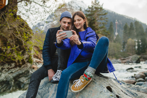 man and woman sitting on rock looking at phone