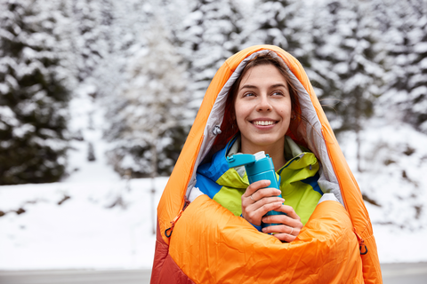 happy woman in orange sleeping bag with blue thermostat in hand