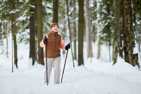 old woman walking in snow covered woods with trekking poles