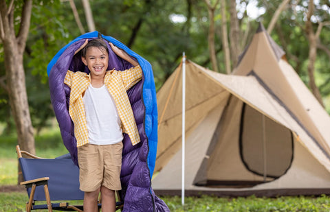 young child holding sleeping bag over head at campsite