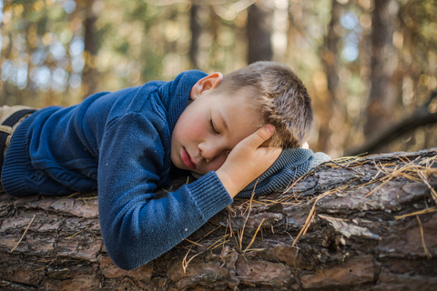 young boy sleeping on log of wood