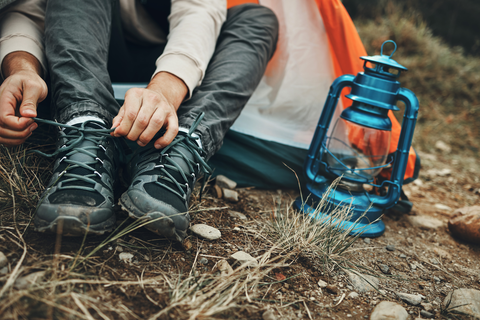 hands tying up hiking shoes while sitting on forest floor