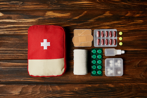 A red first aid kit with all the items on the side on a wooden table