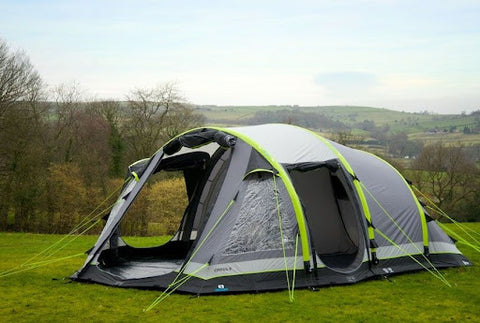 A green and grey inflatable tent on some grass with fields in the background