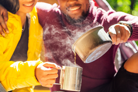 man and woman smiling in warm clothes pouring warm drink into cup