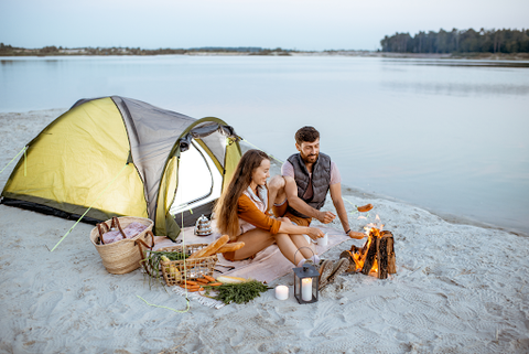 A couple on some beach sand with their tent next to the river