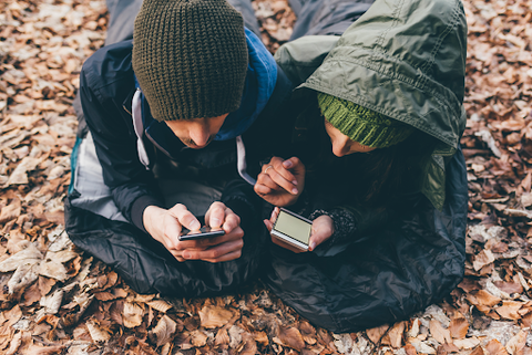 A couple lying next to each other in their bivy sacks looking at their phones