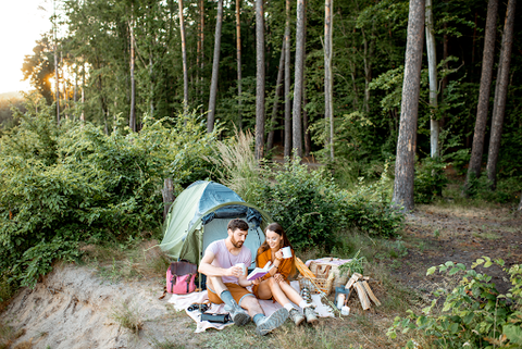 A couple outside their  backpacking tent in the forest with their personal things next to them