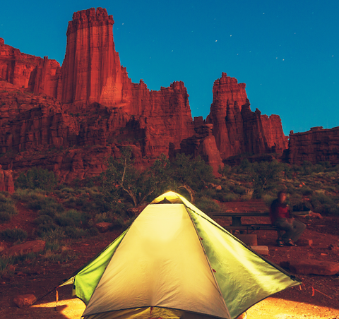 A pyramid tent that is glowing yellow in the rocky mountains