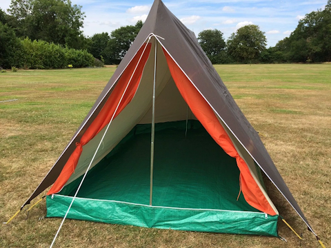 An orange and grey tent with a green groundsheet in a field with trees in the background