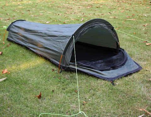 A dark green grey bivy tent that is pitched on the grass