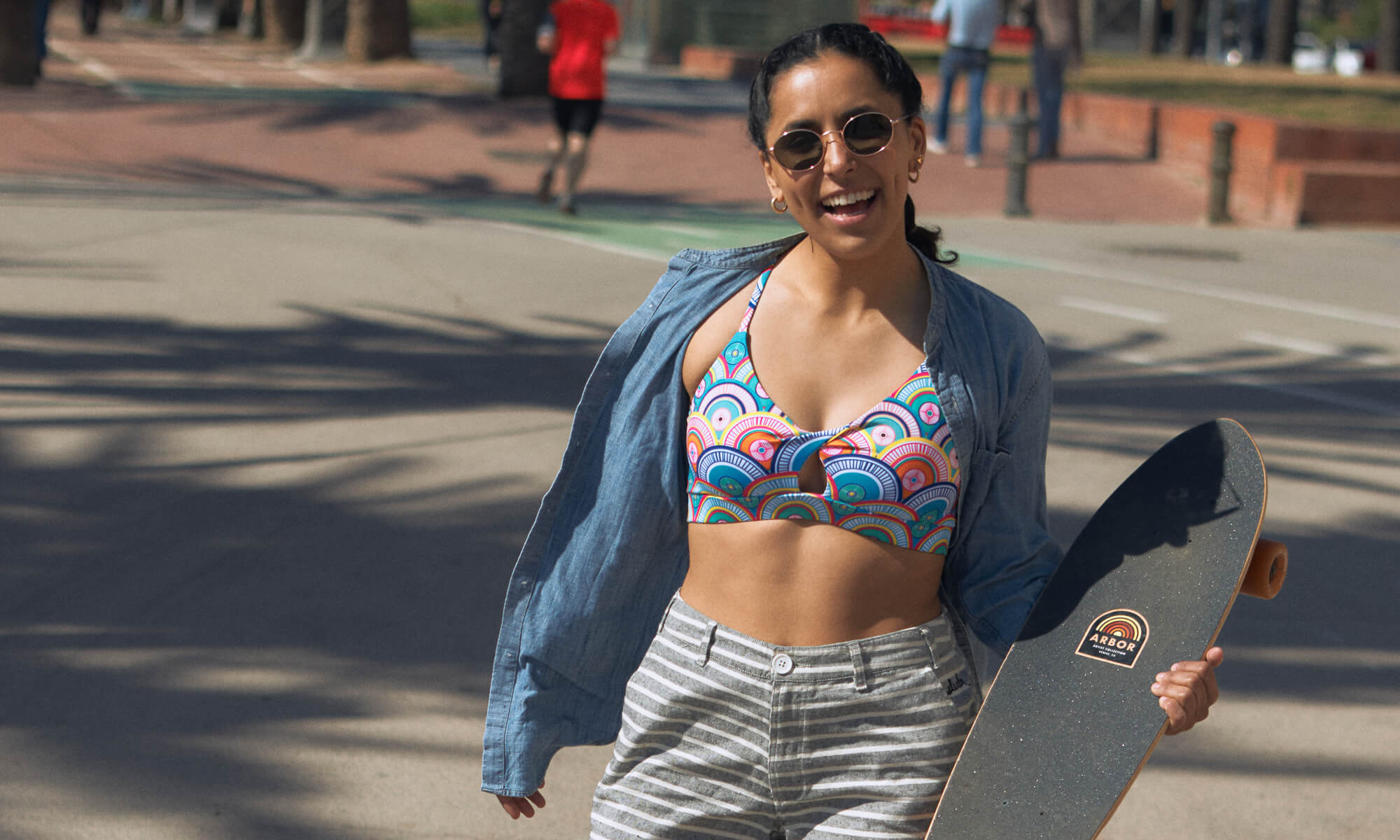 Woman wearing a multicolor print with circle motifs, holding a skateboard and smiling in Barcelona