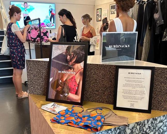 inside of a fashion boutique in SoHo NYC, framed signs say Rubisnacks Barcelona while customers look at colorful printed sports bras on a clothing rack