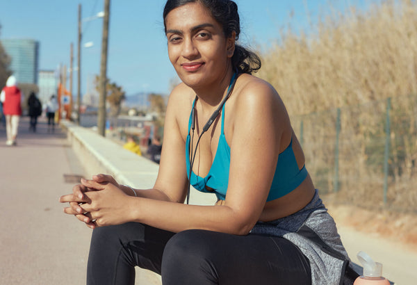 woman wearing a teal sports bra in running clothes and sitting down on the side of a path