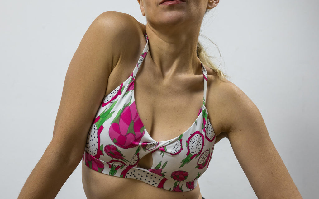 Close up of a woman wearing a sports bra that is white with Pitaya or Dragon Fruit print in pink and green
