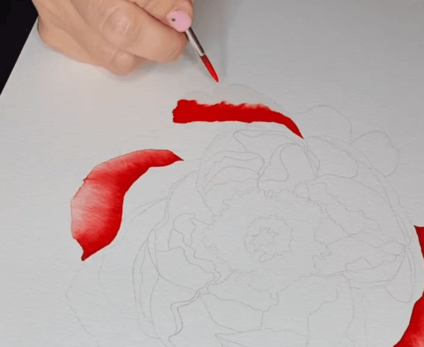 a hand painting a flower with red watercolors