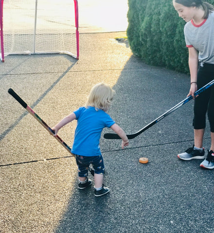 Teen girl playing hockey with toddler 