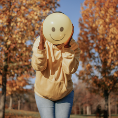 Woman holding balloon with smiley face over face