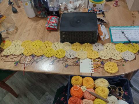 Temperature blanket made of yellow crocheted hexagons laying out on a hand-painted table. 
