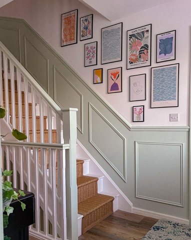 Green traditional panelling up staircase with colourful prints