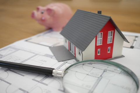 A magnifying glass, model house, and piggy bank on top of a floorplan. 