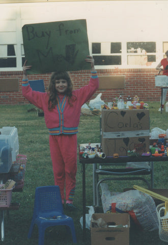 Photo of 7 year old me holding a sign that says "buy from me" at our school yard sale