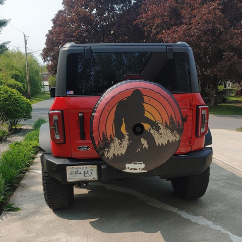 Retro Sasquatch and Ford Bronco spare tire cover on a red Ford Bronco