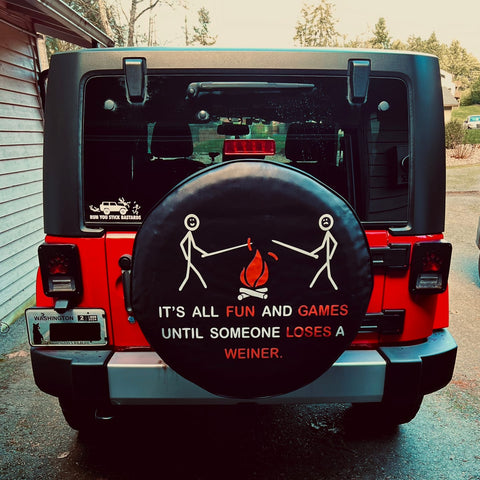 Funny spare tire cover of stick figures roasting hot dogs over a campfire and saying it is all fun and games until someone loses a weiner