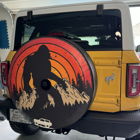 Retro Sasquatch and Ford Bronco spare tire cover on a yellow Ford Bronco