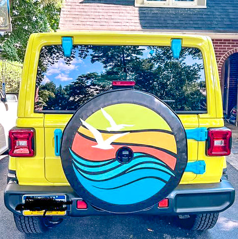 Yellow Jeep Wrangler showing a beach and wave spare tire cover with a back up camera hole