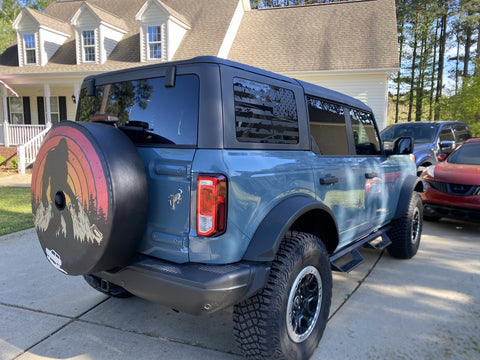 Blue Ford Bronco and a Sasquatch spare tire cover design in a driveway