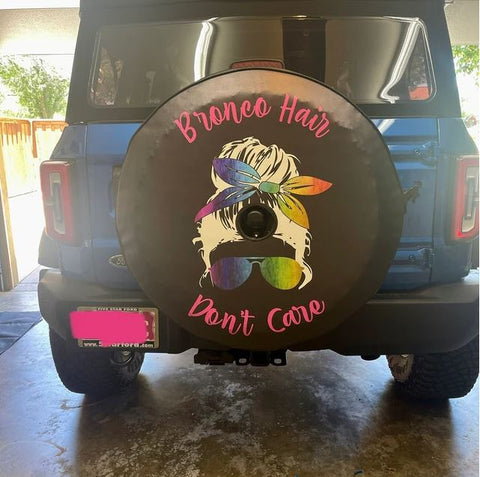 Teal Ford Bronco with a custom spare tire cover design of a messy bun decal with rainbow coloring and the quote, "bronco hair don't care"