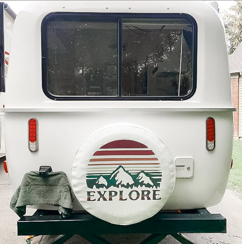 White camper van and a white vinyl camper spare tire cover that says Explore with mountains