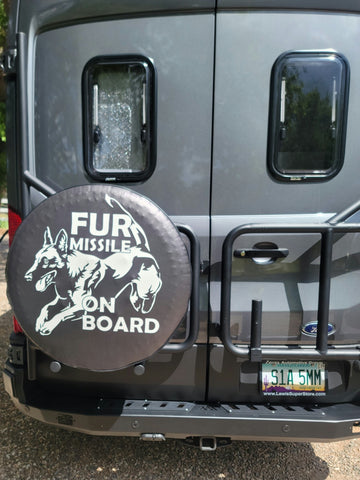 A gray sprinter van with a black vinyl spare tire cover that says fur missile and has an image of a Belgian Malinois