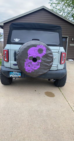 Gray Ford Bronco with a custom spare tire cover design of a purple skull and floral design.