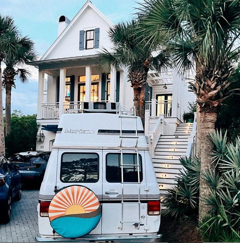 Retro sunset with sun rays shining out over the turquoise ocean spare tire cover on a conversion van in a driveway of a large coastal home. 
