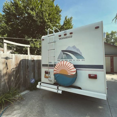 Older Winnebago RV with a vintage sun rays and water designed spare tire cover