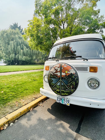 A VW bus with a spare tire on the front that is covered with a pretty peace sign design