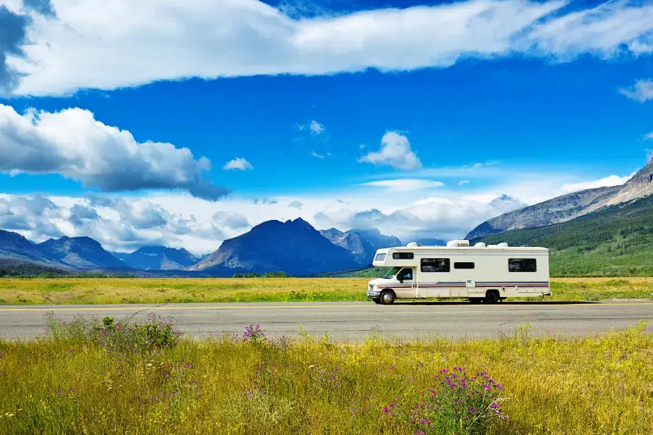 a zoomed out image of an RV driving down the road on a beautiful blue sky day in the mountains