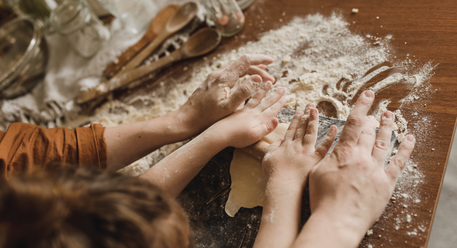 A child and caregiver patting dough on countertop