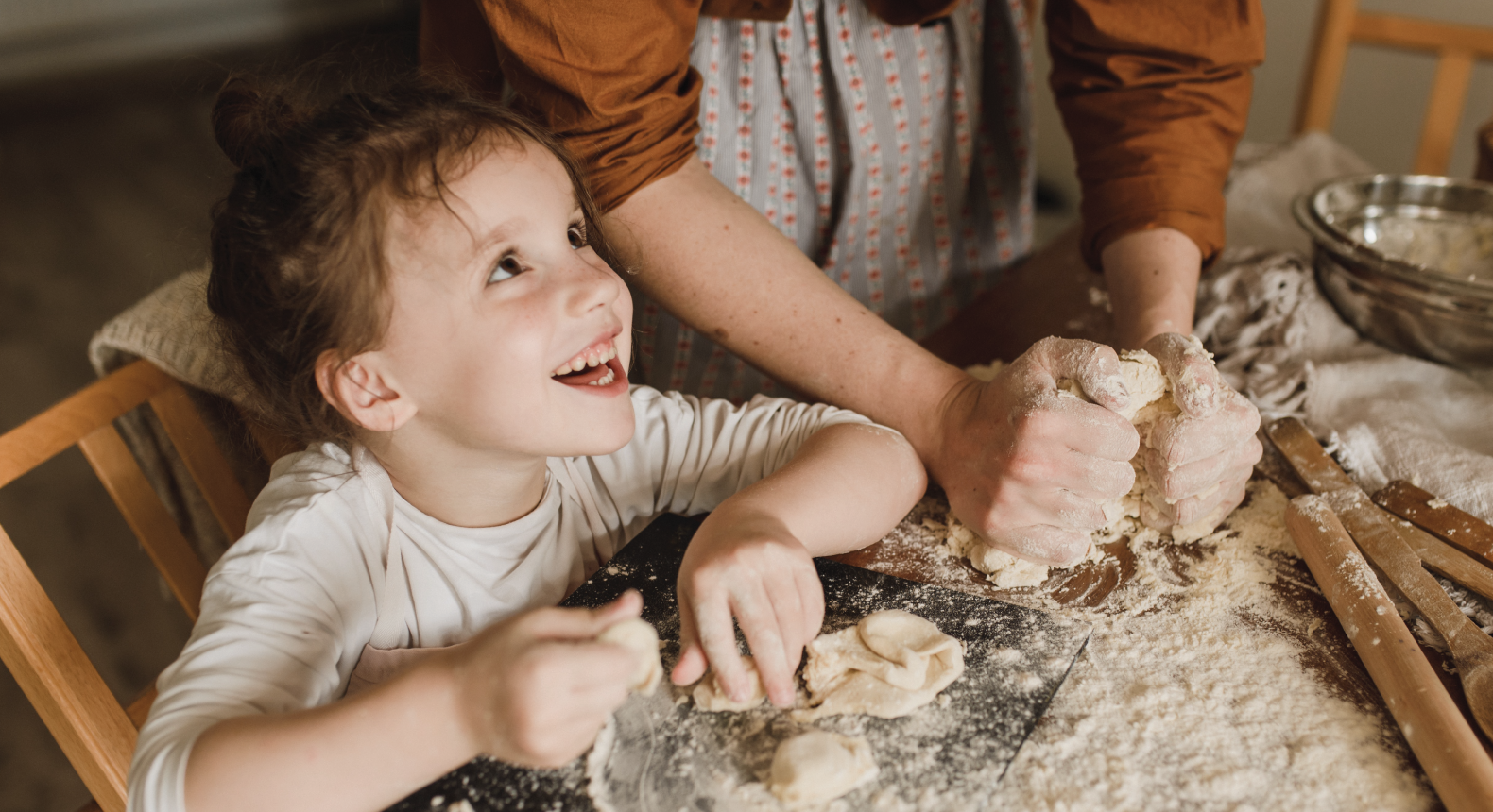 A child looks up from the dough with a smile