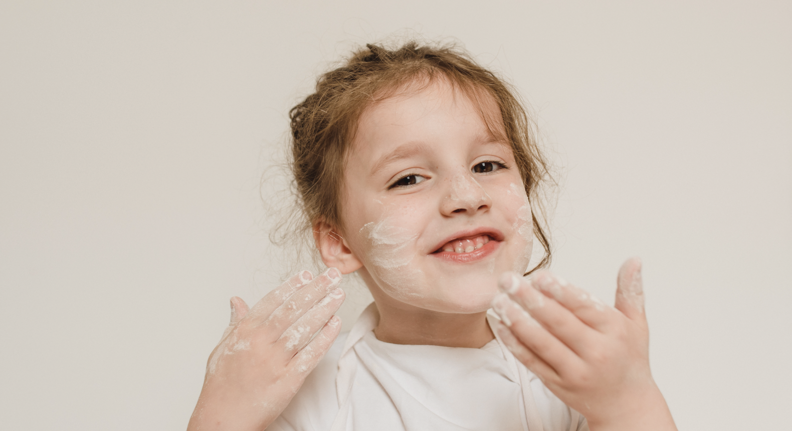 A child holding up their hands with flour on face and hands