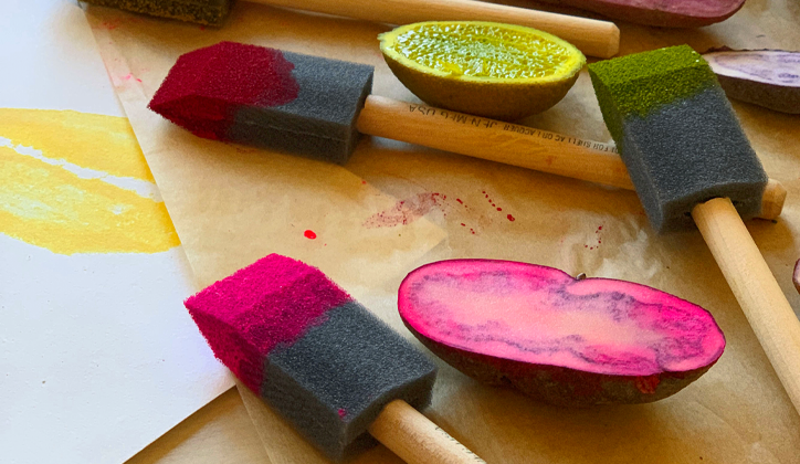 Foam brushes with pink and green paint on them with fruit and vegetable stamps on a table