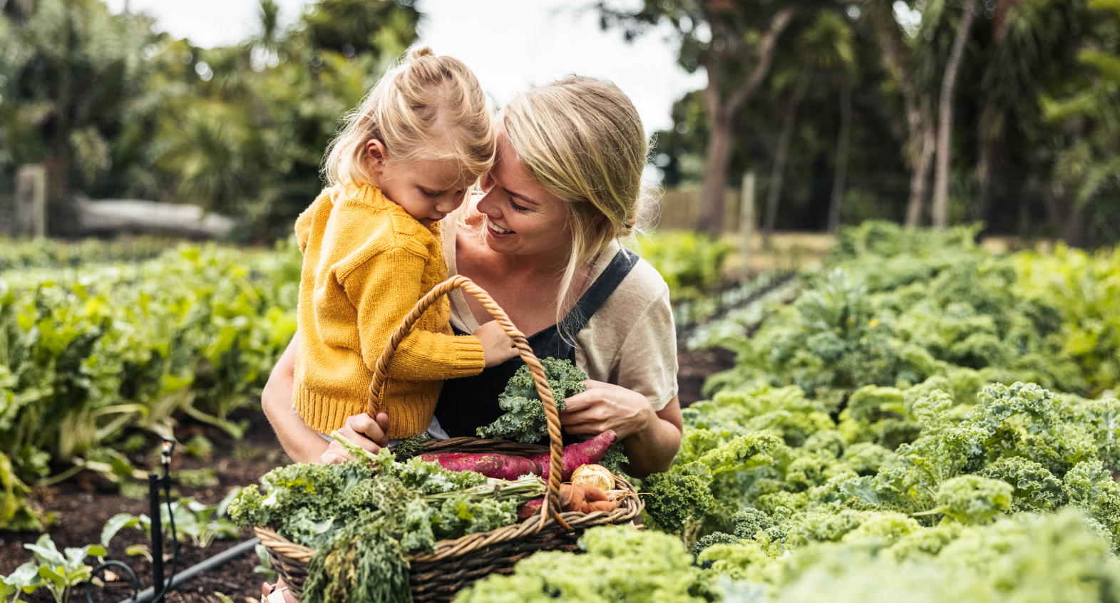 a child and caregiver with a basket of fresh greens in a garden